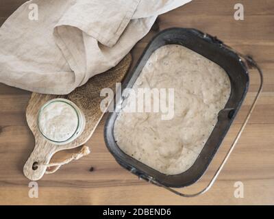 Weizensauerteig Starter im Glasgefäß und Sauerteig in der Brotpfanne der Brotmaschine. Hausgemachtes Brotbackkonzept Stockfoto