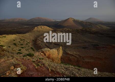 Wunderschöne Vulkanlandschaft am frühen Morgen auf Lanzarote, Spanien. Der Calima Wind macht ein surreales Licht. Weit weg im Hintergrund das kleine Schlepptau Stockfoto