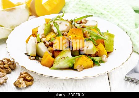 Salat aus gebackenem Kürbis, frischer Birne, Rucola und Walnüssen, gewürzt mit Honig, Balsamico-Essig, Gewürze und Pflanzenöl auf einem Holzbrett BA Stockfoto