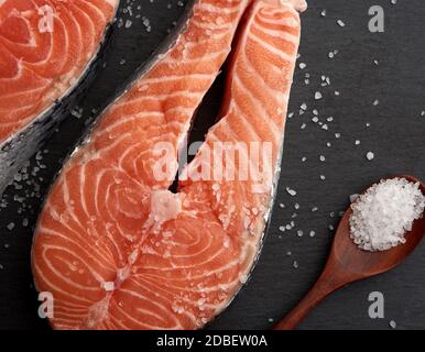 Rohe Lachssteaks mit weißem Salz auf schwarzem Hintergrund, Draufsicht Stockfoto