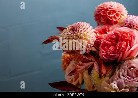 Florale Komposition von Dahlia Blumen, Rosen und Blätter im Herbst. Arty, leuchtend rot und rosa Blumenstrauß auf blauem Hintergrund Stockfoto