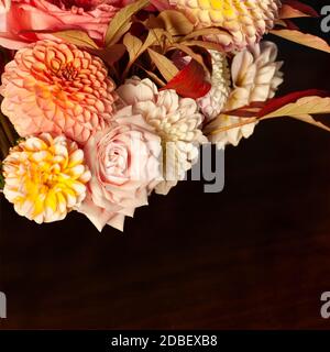 Florale Komposition aus Dahlia-Blüten, Rosen und Herbstblättern. Arty, leuchtend rot und rosa Farbe Bouquet von Blumen auf dunklem Hintergrund Stockfoto