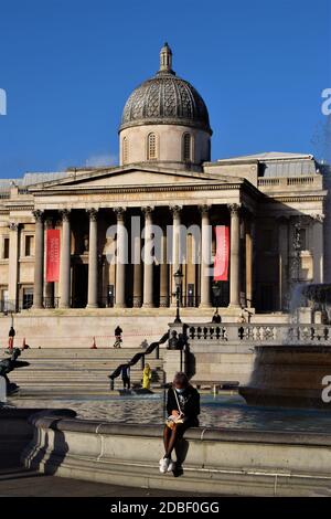 London, Großbritannien. November 2020. Eine Frau mit Gesichtsmaske sitzt vor der National Gallery am Trafalgar Square.die meisten Plätze haben geschlossen, da die zweite Monat lange nationale Sperre in England greift. Kredit: SOPA Images Limited/Alamy Live Nachrichten Stockfoto