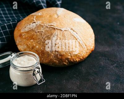 Sauerteig Vorspeise und Weizensauerteig Brot. Weizen sauren Teig Starter im Glas und köstliche hausgemachte runde Sauerteig Brot auf schwarzem Hintergrund, CO Stockfoto