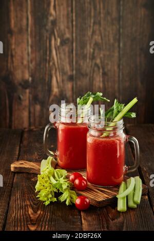 Zwei Gläser mit frischem Tomatensaft, Sellerie, Petersilie und reifen Tomaten auf dunkelbraunem Holzhintergrund. Gesundes Getränk, Gemüsesaft Stockfoto