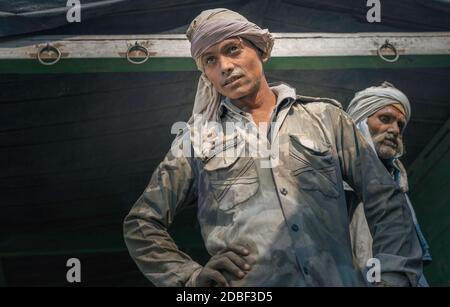 Arbeiter, die mit schweren Zementsäcken vom Eisenbahnzug zum wartenden Lastwagen, Mathura, Uttar Pradesh, Indien, beschäftigt sind. Stockfoto