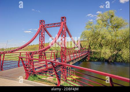 Schöne eisenrote Hängebrücke über den kleinen Fluss Irpin von der Promenade zum grünen Wald. Stockfoto