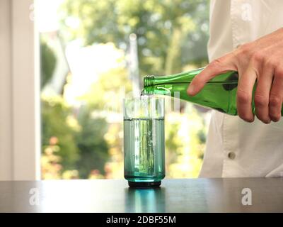 Mann mittleren Alters gießt Wasser in ein Glas, gesundes Essen Konzept, sauber und frisch Stockfoto