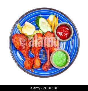 Indische Küche - Draufsicht auf die Portion Tandoori-Huhn (würzige Hähnchenschenkel, mariniert in Joghurt und Gewürzen und in Tandoor geröstet) mit Saucen auf blu Stockfoto