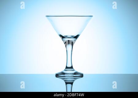 Leeres martini-Glas steht auf einem glänzenden Tisch mit Spiegelung. Kaltblaue getönte Vignette. Stockfoto