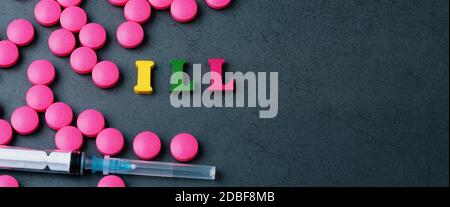 Eine Inschrift auf einem grauen Hintergrund, umgeben von leuchtend rosa Pillen und einer weißen Spritze aus einem weißen Glas verstreut. Das Konzept der Behandlung und PR Stockfoto