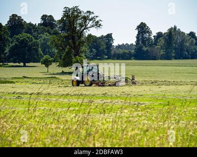Traktor mäht Gras auf einem großen Feld auf einem Land Anwesen mit Bäumen im Hintergrund Stockfoto