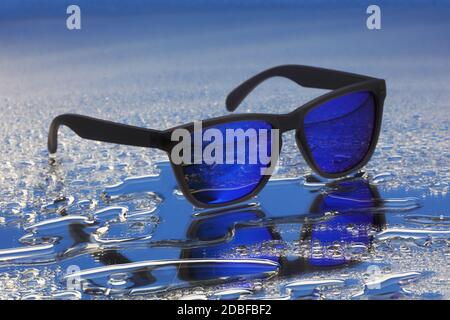Blaue Sonnenbrille mit schwarzen Rahmen auf Wassertropfen Reflexion mit Selektiver Fokus Stockfoto
