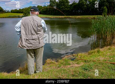 Lincolnshire, Großbritannien - Herr Barry Grantham, ein Ausbilder in Fliegenfischen, wirft eine Fliegenschnur über einen Forellensee für Regenbogenforelle Stockfoto