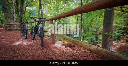 Zwei Mountainbikes auf einem Holzzaun neben einem schönen kleinen See auf einem grünen Waldweg. Mountainbike-Konzept. Freiheit und Erholung c Stockfoto