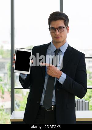 Geschäftsleute in Anzügen und Krawatten, die mit dem Finger auf einen Tablet-Computer mit leerem Bildschirm zeigen. Arbeitsatmosphäre am Morgen in einem modernen Büro. Stockfoto