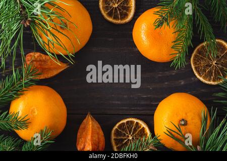 Frische und getrocknete Mandarinen mit Kiefer- und Fichtenzweigen, Physalis-Nahaufnahme in einem Rahmen angeordnet. Platz in der Mitte kopieren. Postkarte für Weihnachten und Stockfoto