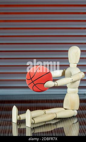 Holzpuppe mit Basketball vor einem Jalousie spielt mit dem Ball Stockfoto