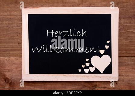 Balckboard Mit Deutschem Text Herzlich Willkommen Bedeutet Willkommen Rustikale Holzherz Dekoration. Brauner Holzhintergrund Stockfoto