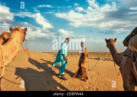 Rajasthan Reise Hintergrund - zwei indische Kamele (Kameltreiber) mit Kamelen in den Dünen der Thar Wüste. Jaisalmer, Rajasthan, Indien Stockfoto