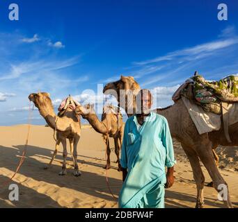 Rajasthan Reise Hintergrund - Indischer Mann Kameltreiber Porträt mit Kamelen in den Dünen von Thar Wüste. Jaisalmer, Rajasthan, Indien Stockfoto