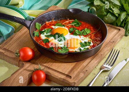 Köstliche Middle East Shakshuka - Spiegeleier, Zwiebel, Paprika, Tomaten, Chili und Gewürze in Gusseisen Steppan mit Küchentuch auf alt Stockfoto