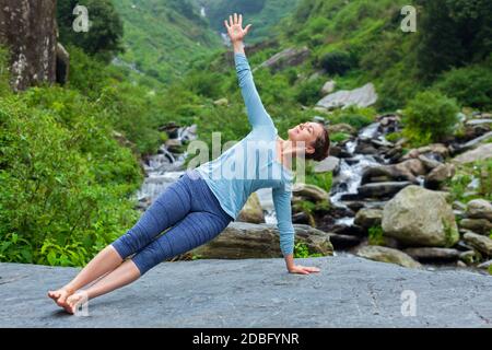 Yoga im Freien - schöne sportliche fit Frau dabei Yoga Asana Vasisthasana - seitliche Plankenstellung am tropischen Wasserfall Stockfoto