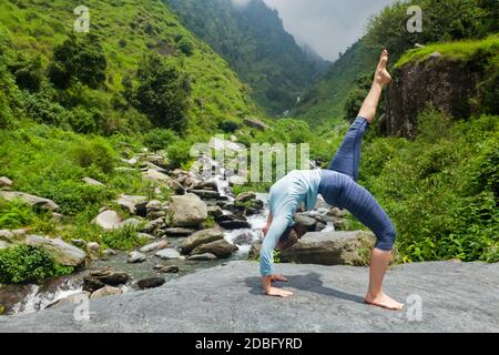 Frau tut Yoga asana eka pada urdva dhanurasana aufwärts Bogen Pose im Freien am Wasserfall im Himalaya Stockfoto
