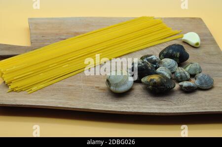 Alles, was Sie brauchen, bereit, appetitliche Spaghetti mit Venusmuscheln mit dem perfekten italienischen Rezept zu kochen, alles auf einem eleganten Schneidebrett aus edlem Woo platziert Stockfoto