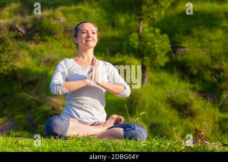 Meditation und Entspannung Yoga im Freien - junge Frau meditieren und Entspannen in Padmasana Lotus Pose mit namaste Anjali Mudra auf Grünes Gras im Vordergrund Stockfoto