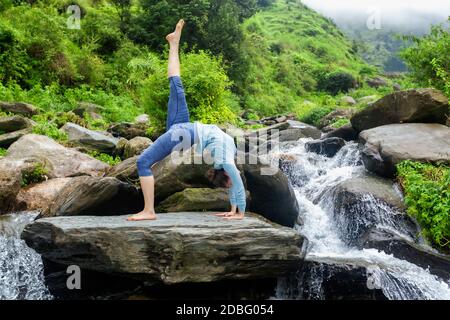 Frau tut Yoga asana eka pada urdva dhanurasana aufwärts Bogen Pose im Freien am Wasserfall im Himalaya Stockfoto