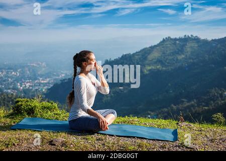 Frau praktiziert Pranayama Yoga Atemkontrolle in Lotus Pose padmasana im Freien im Himalaya am Morgen bei Sonnenaufgang. Himachal Pradesh, Indien Stockfoto