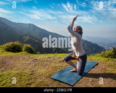 Junge Frau, die Ashtanga Vinyasa Yoga machte, entwickelte schwierige Asana Vatayanasana (Pferdehaltung) im Freien in Himalaya-Bergen. Himachal Pradesh, Indien Stockfoto