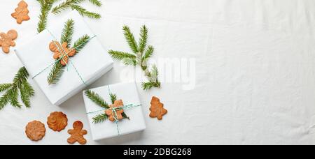 Weihnachtsgeschenke in weißem Papier verpackt und mit Fichte verziert Zweige und Lebkuchen auf einem Stoff Hintergrund Stockfoto