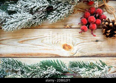 Holzhintergrundrahmen mit verschneiten Tannenzweigen, Weihnachtsbeeren und Tannenzapfen. Neujahr Design, kopieren Raum Stockfoto