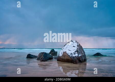 Felsen mit Schnee bedeckt am norwegischen Meer Strand in Fjord bei stürmischem Wetter mit Wolken. Skagsanden Strand, Flakstad, Lofoten Inseln, Norwegen. Lange Ausr Stockfoto