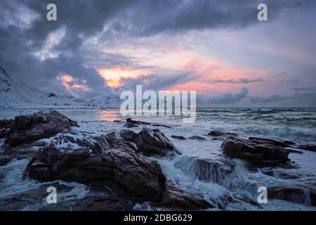 Wellen des norwegischen Meeres an der felsigen Küste im Fjord bei Sonnenuntergang. Skagsanden Strand, Lofoten Inseln, Norwegen Stockfoto