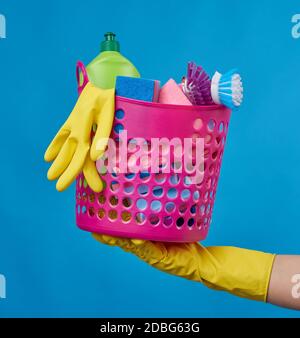 Handgriff rosa Korb mit Waschschwämmen, Gummi-Schutzhandschuhe, Bürsten und Reinigungsmittel in einer grünen Kunststoffflasche auf blauem Hintergrund, Set Stockfoto