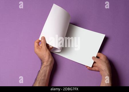 Männliche Hand öffnete einen Katalog auf lila Hintergrund, Mock-up-Serie Vorlage bereit für Ihre Design-Auswahl-Pfad enthalten Stockfoto
