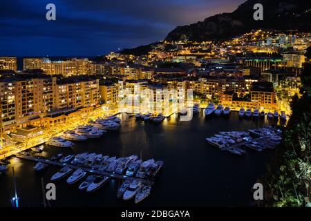 Luftaufnahme des Hafens von Monaco Monte Carlo und der beleuchteten Skyline der Stadt in der Abenddämmerung. Monaco Port Nachtansicht mit luxuriösen Yachten Stockfoto