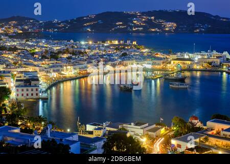 Blick auf die Stadt Mykonos griechisches Urlaubsziel mit berühmten Windmühlen und Hafen mit Booten und Yachten, die abends blau beleuchtet sind Stockfoto