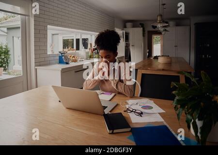 Frau allein sitzen Blasen Nase während mit Laptop während der Arbeit Von zu Hause aus Stockfoto