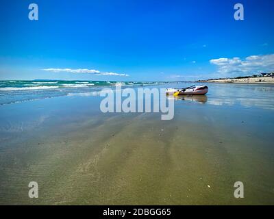 Schlauchboot an einem abgelegenen Strand mit Reflexion, blauem Himmel und krebierenden Wellen. Perfektes Reisebild für einen ruhigen und friedlichen Strand Stockfoto