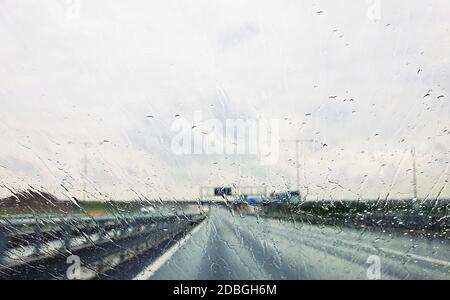 Ein Blick vom Auto durch das Fenster mit Regentropfen während der Fahrt. Fahren eines Autos im Regensturm auf der Autobahn. Stockfoto