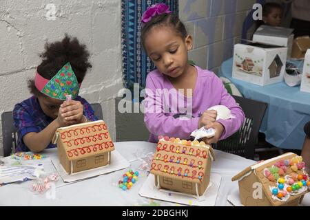 Unterprivilegierte Kinder bauen und dekorieren Lebkuchenhäuser auf einer Weihnachtsfeier in einem Gemeindezentrum in Manhattan, New York City. Stockfoto