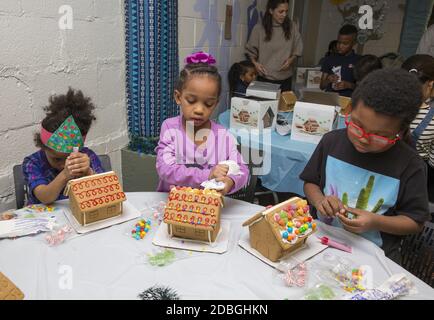 Unterprivilegierte Kinder bauen und dekorieren Lebkuchenhäuser auf einer Weihnachtsfeier in einem Gemeindezentrum in Manhattan, New York City. Stockfoto