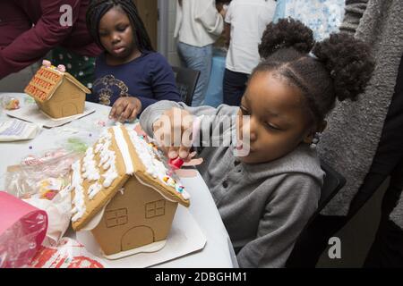 Unterprivilegierte Kinder bauen und dekorieren Lebkuchenhäuser auf einer Weihnachtsfeier in einem Gemeindezentrum in Manhattan, New York City. Stockfoto