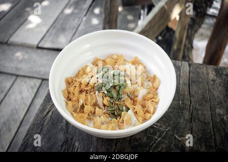 Gesundes Frühstück Obstschale mit Banane, Cornflakes, Kürbiskerne und Kokosmilch auf rustikalem Holztisch im Freien Stockfoto