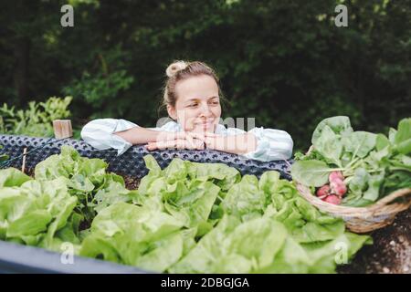 Schöne Frau posiert neben erhöhten Gartenbeet und ihr frisches Gemüse Stockfoto