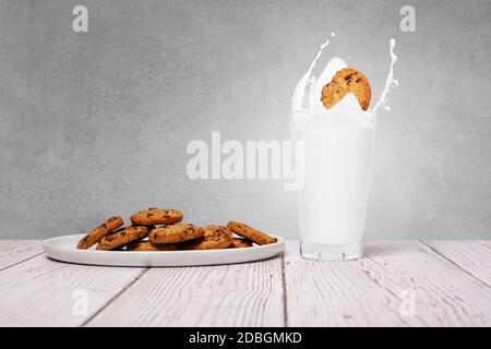 Chocolate Chip Cookie spritzt in ein volles Glas Milch mit Cookies auf der Seite auf einem texturierten Wandhintergrund mit Platz und Platz für Text kopieren Stockfoto